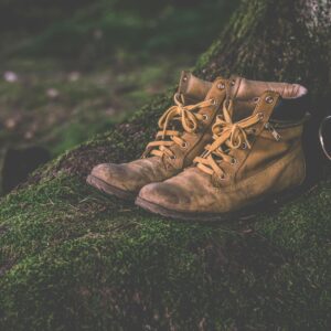 Brown leather hiking boots and cup on a moss-covered forest background, evoking adventure.