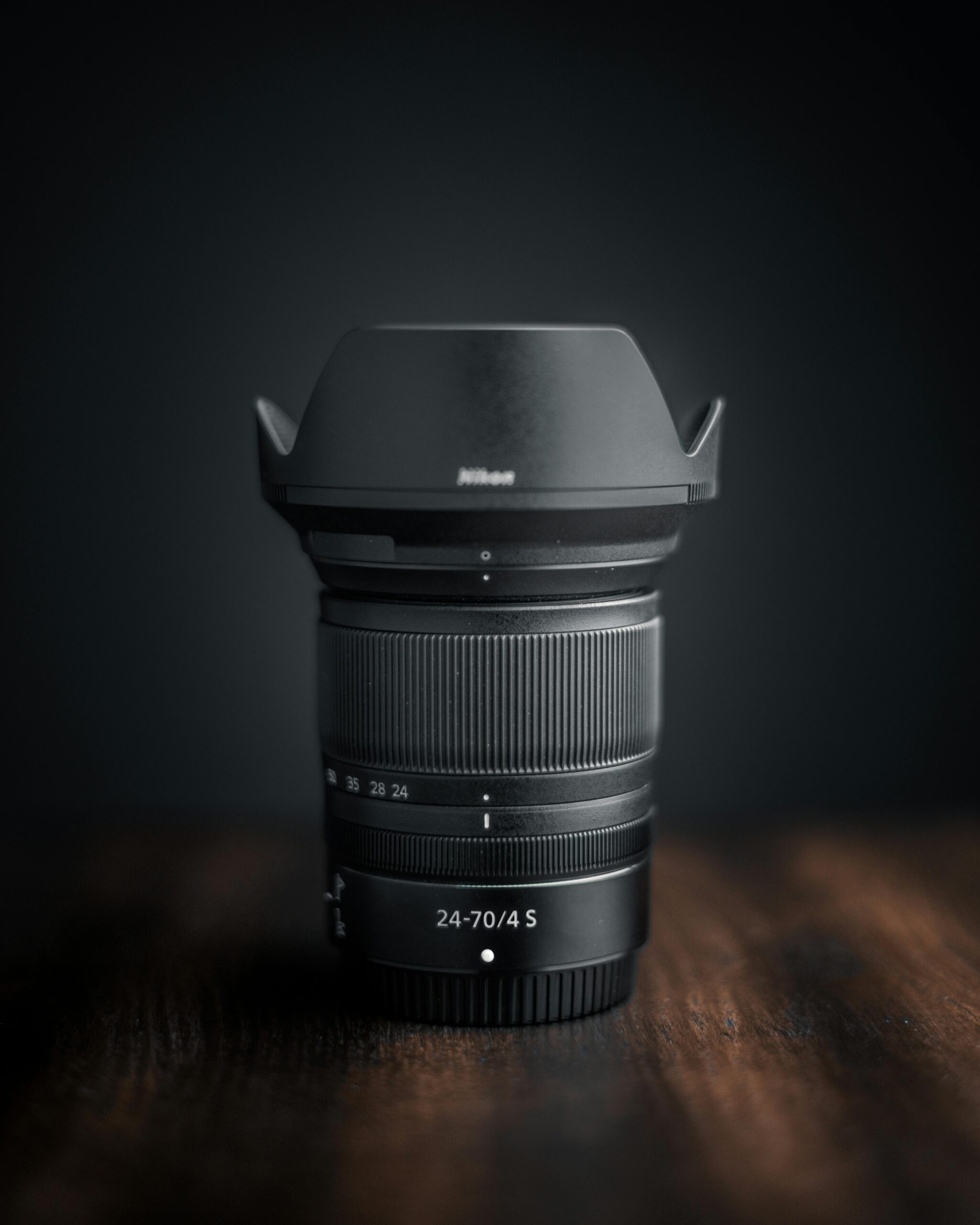 Detailed photo of a Nikon camera lens on a dark wooden surface, showcasing modern technology.